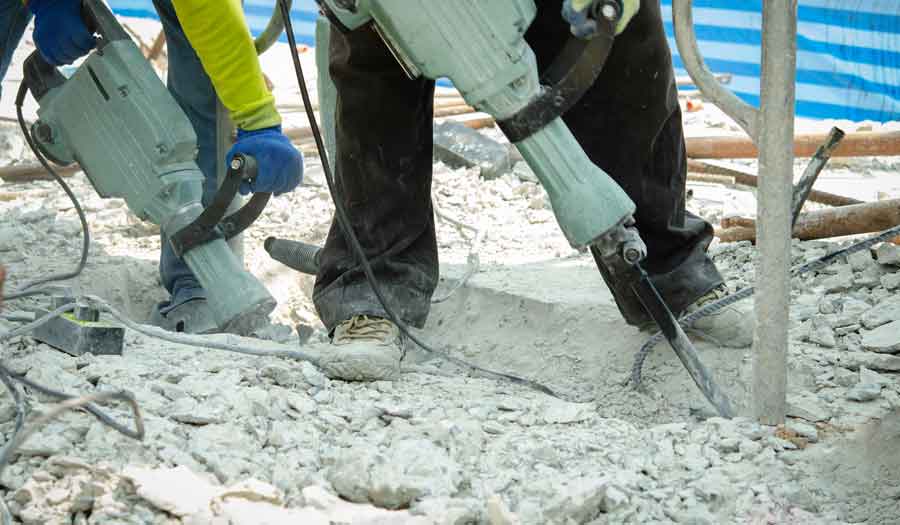 Workers using jackhammer to break apart concrete floor