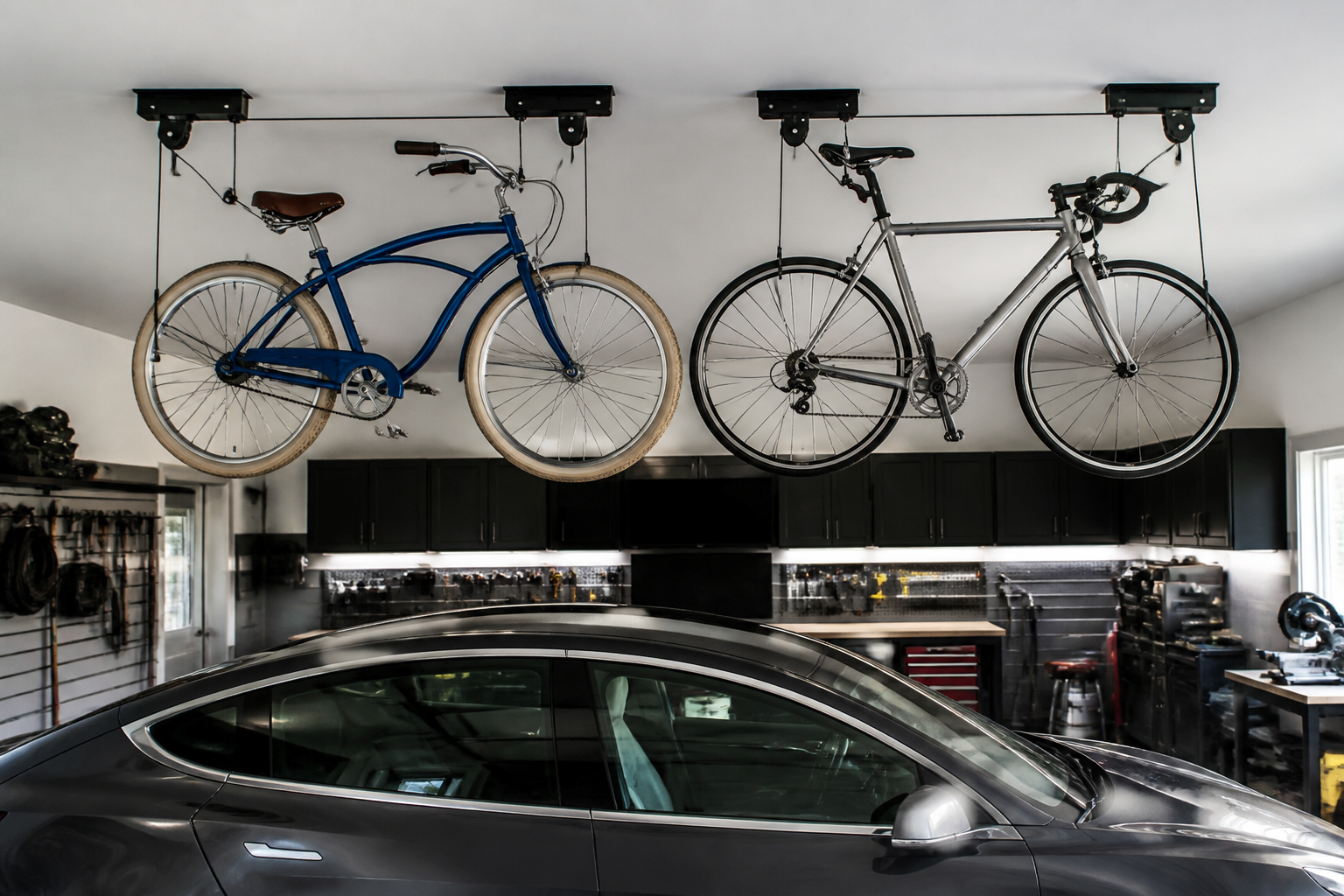 Double ceiling hoist system with two bikes suspended over parked car in garage