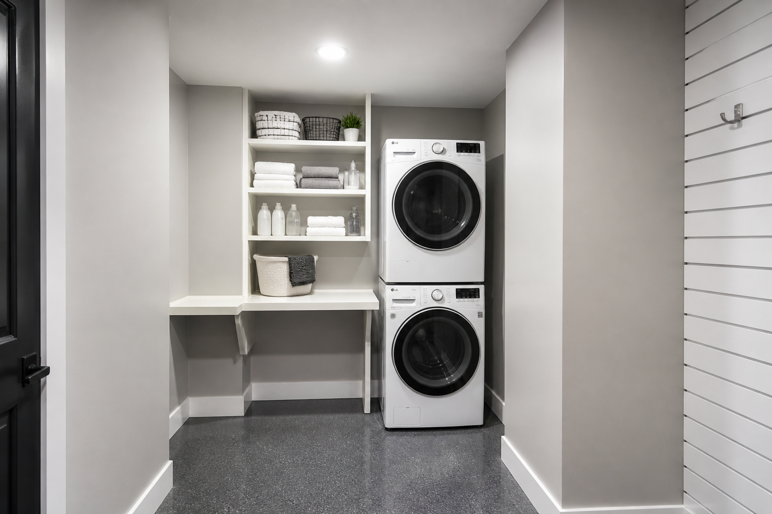Compact stackable washer dryer in garage corner with white shelving and folding counter