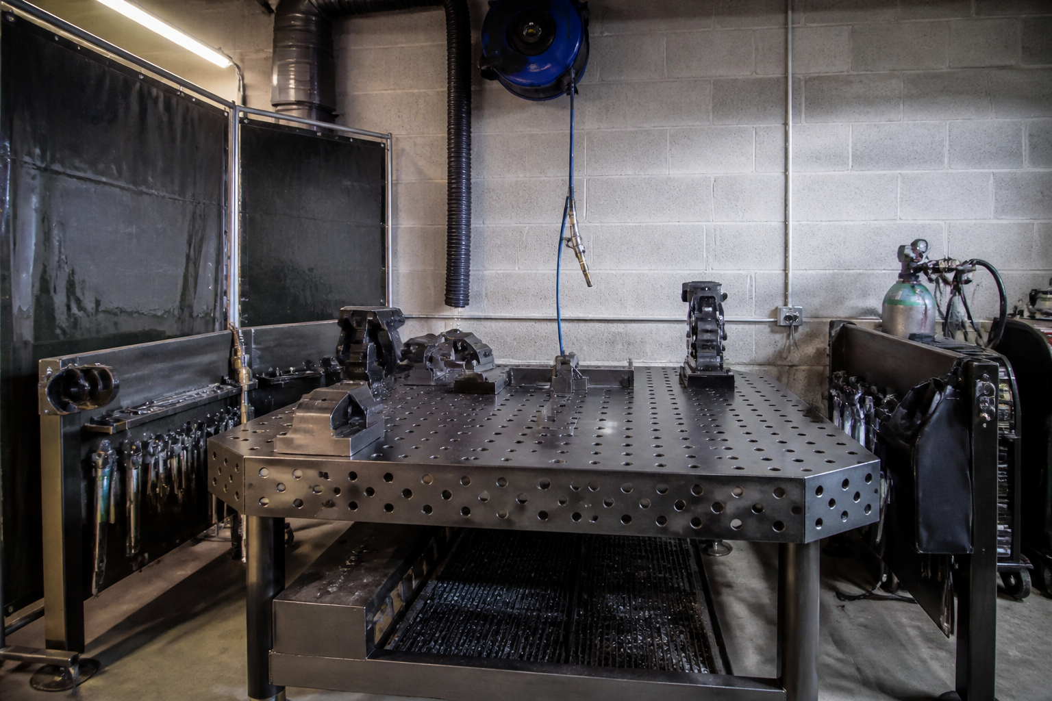 Perforated steel fabrication bench with multiple vises and pneumatic tool access in garage