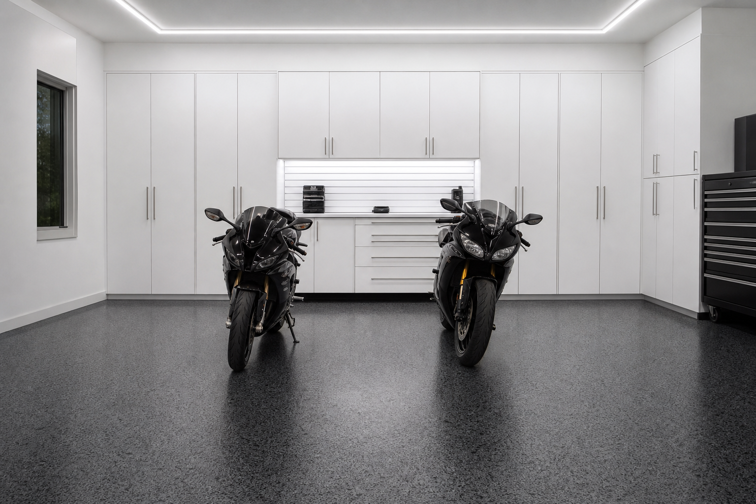 Dark charcoal epoxy garage floor with black and gray flakes and white cabinets and motorcycles