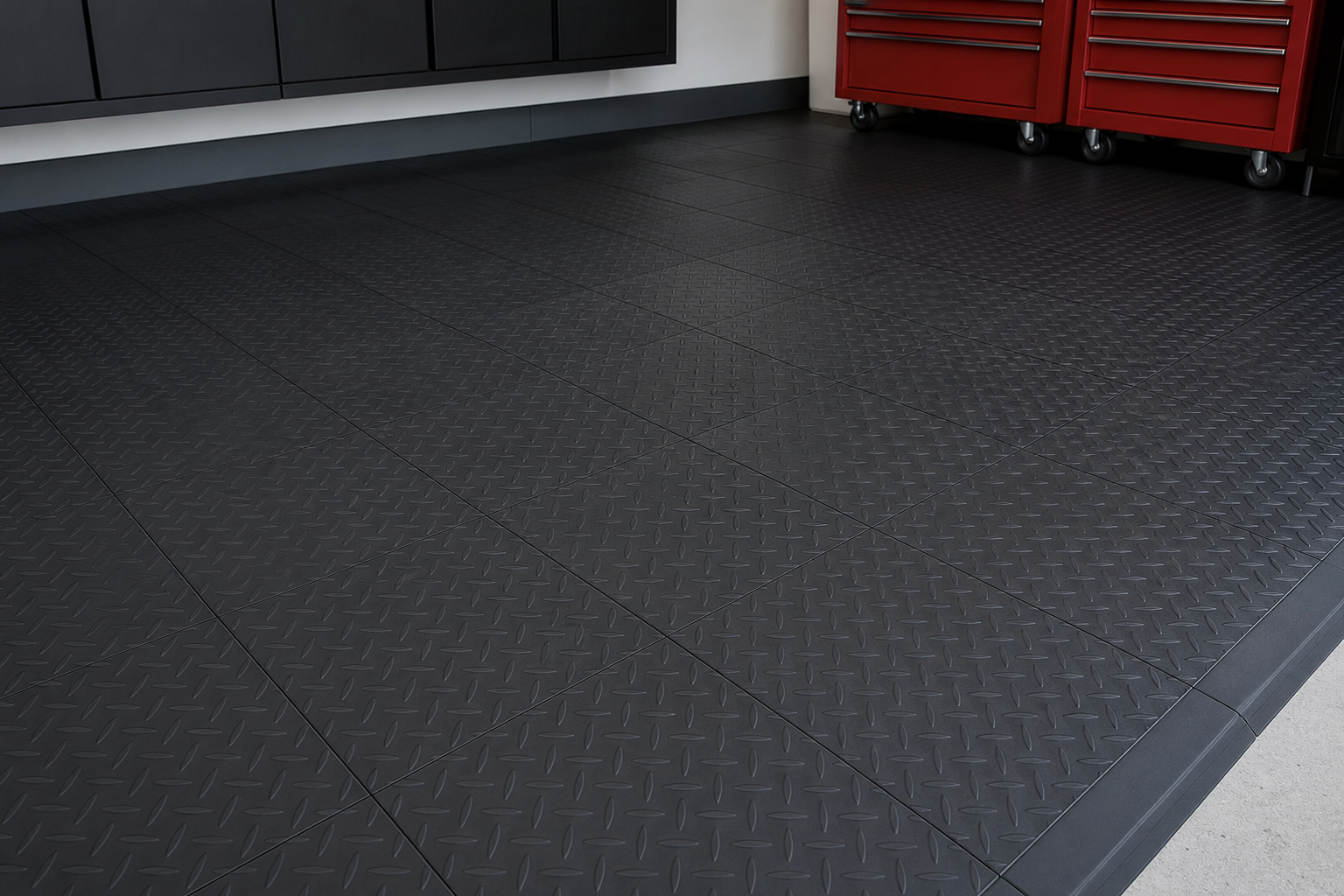 Matte black diamond-plate interlocking garage floor tiles with red toolbox in corner