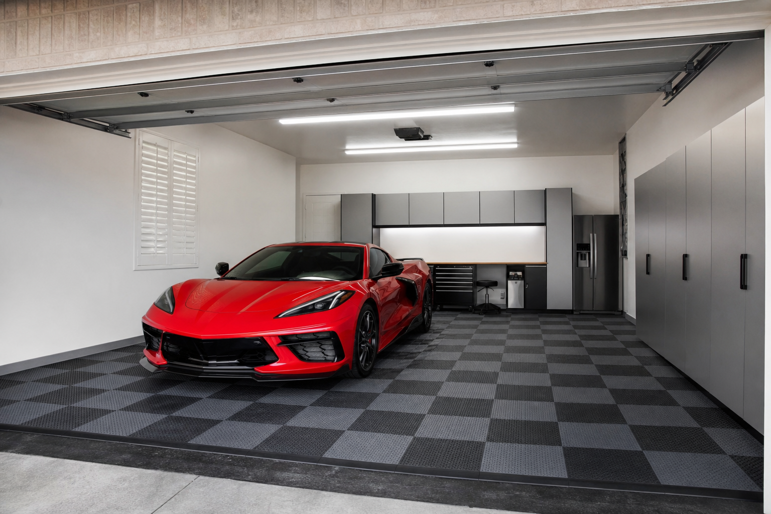 Interlocking gray and black checkerboard rubber floor tiles in a two-car garage with red car