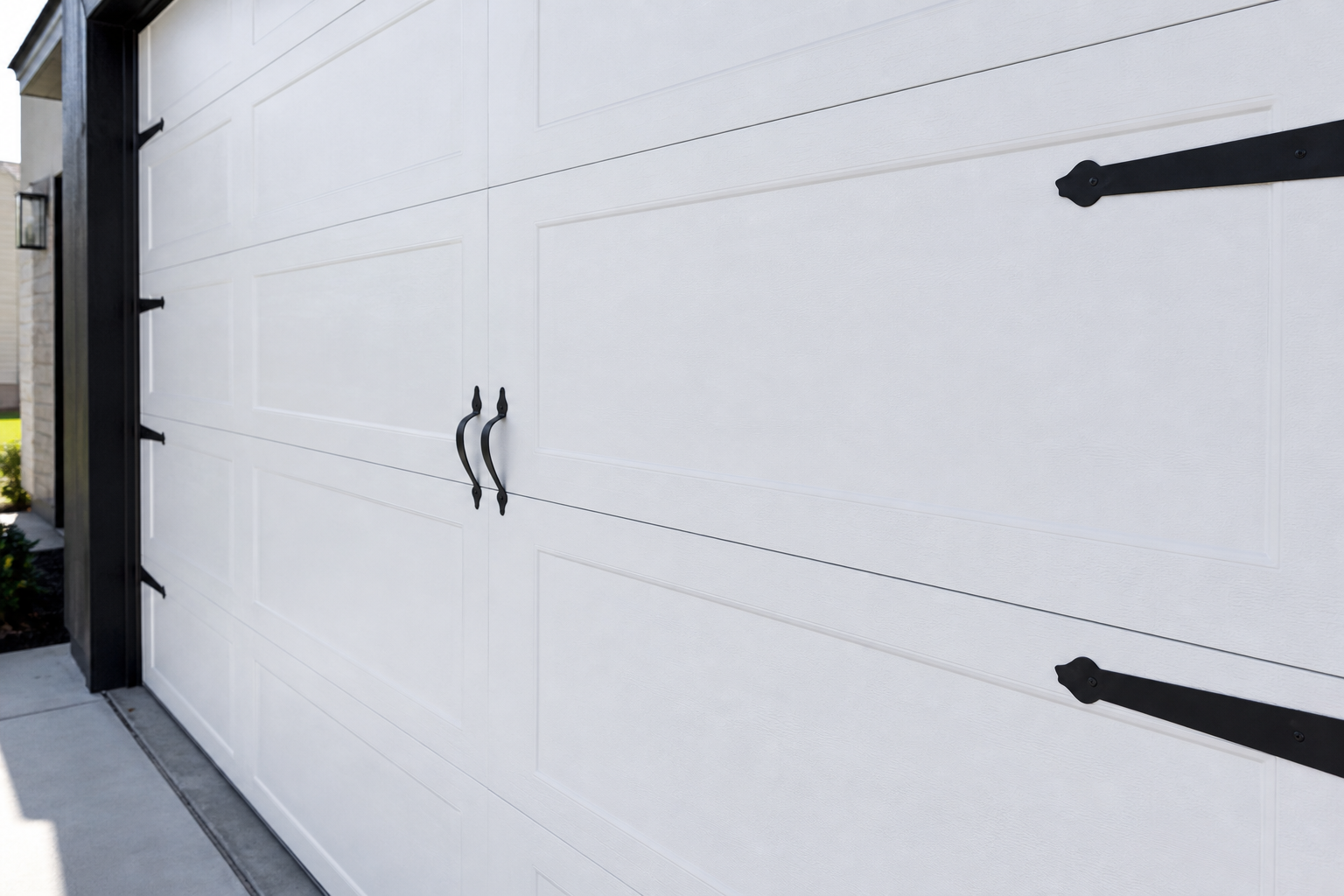 Freshly painted matte black hinges and handles on white garage door panels in sunlight