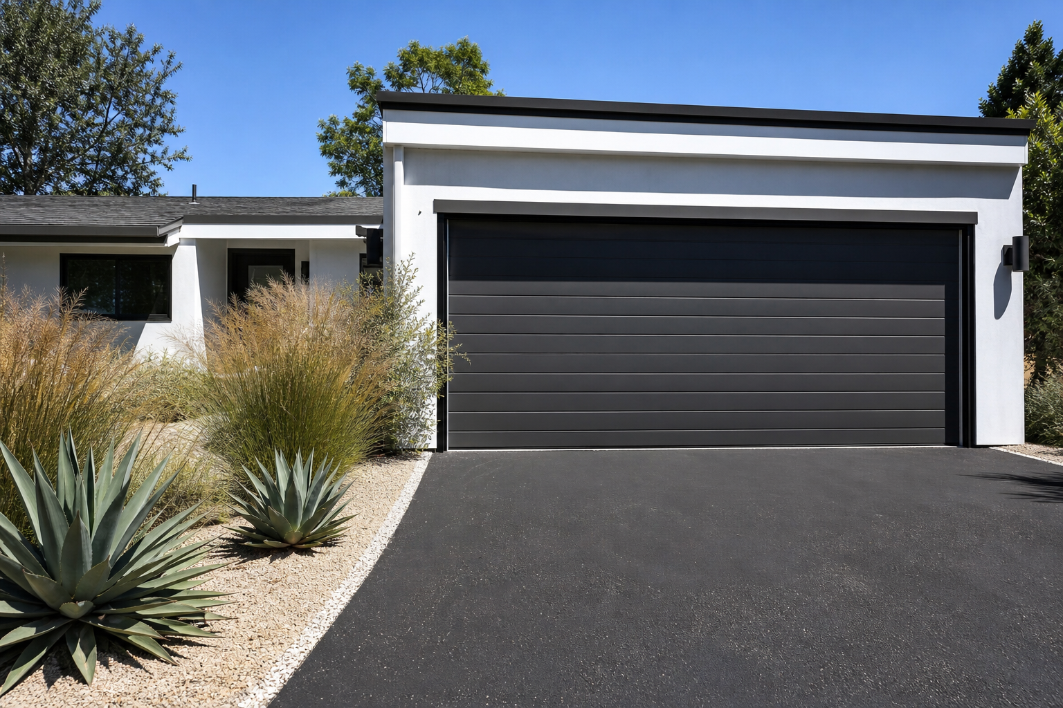 White decomposed granite driveway border with ornamental grasses beside a charcoal modern garage door