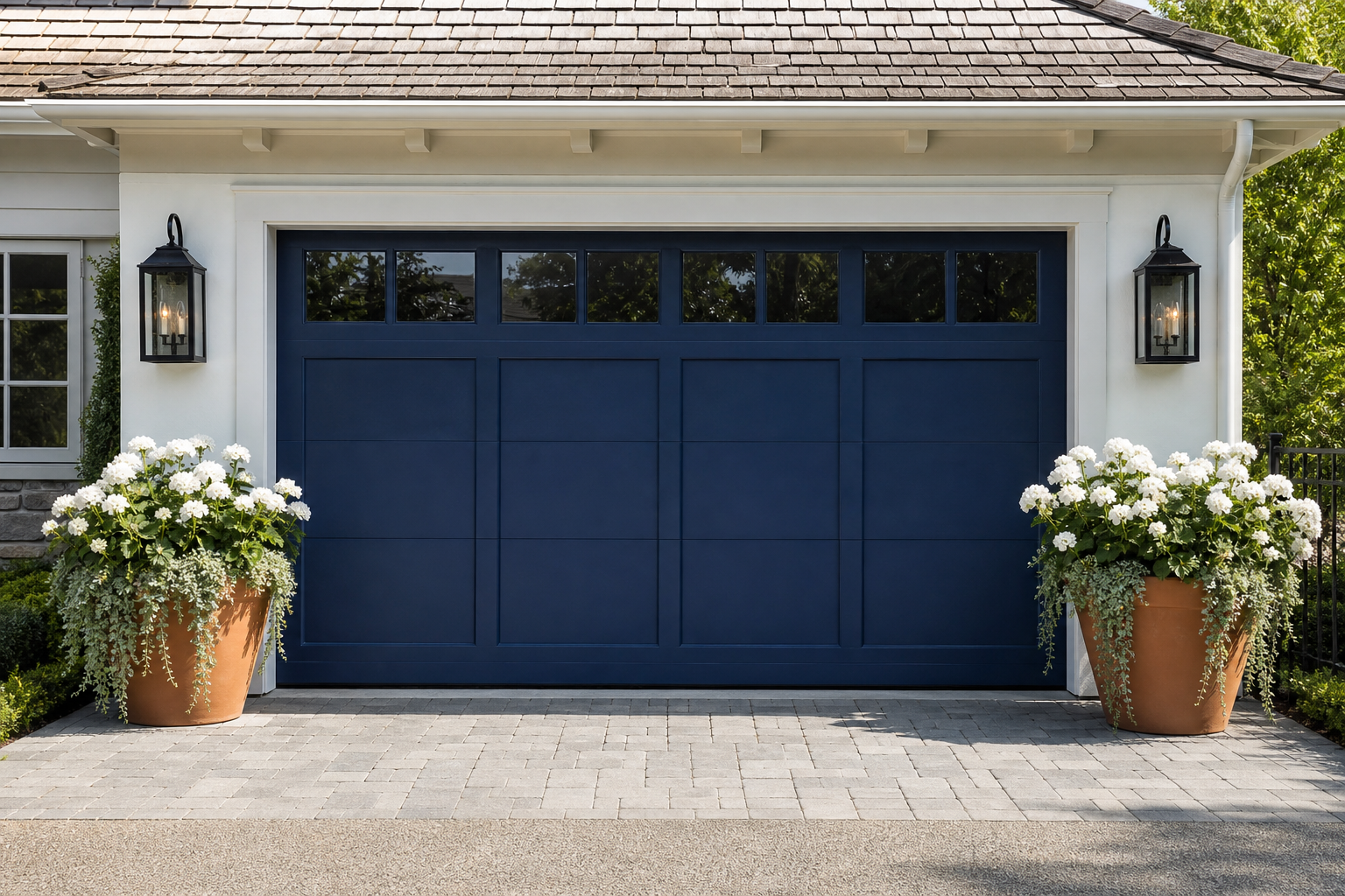 Symmetrical terracotta pots with white geraniums and trailing ivy flanking a navy blue garage door
