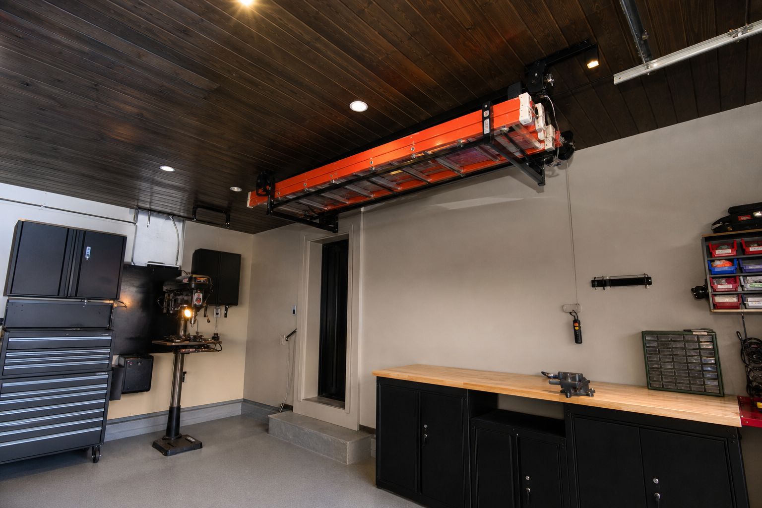 Red fiberglass ladder lifted to tongue-and-groove wood garage ceiling with electric motorized hoist