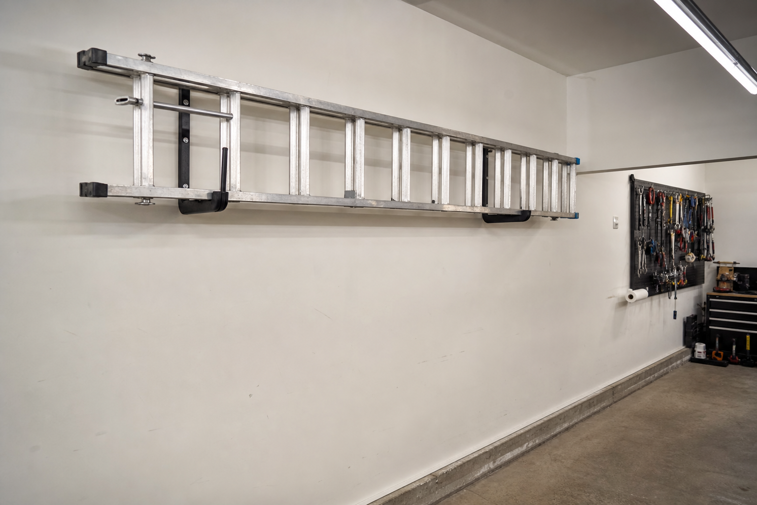 Black J-hook wall brackets holding aluminum extension ladder horizontally on white garage wall