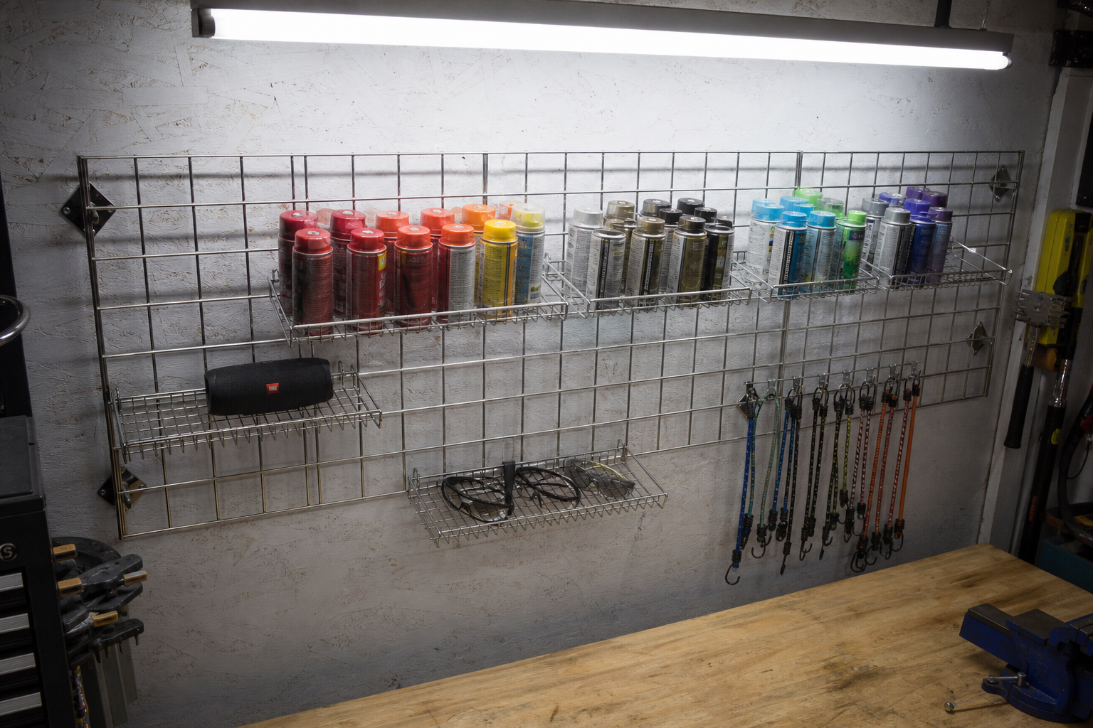 Chrome wire grid wall panel system with adjustable shelves holding spray cans and garage supplies