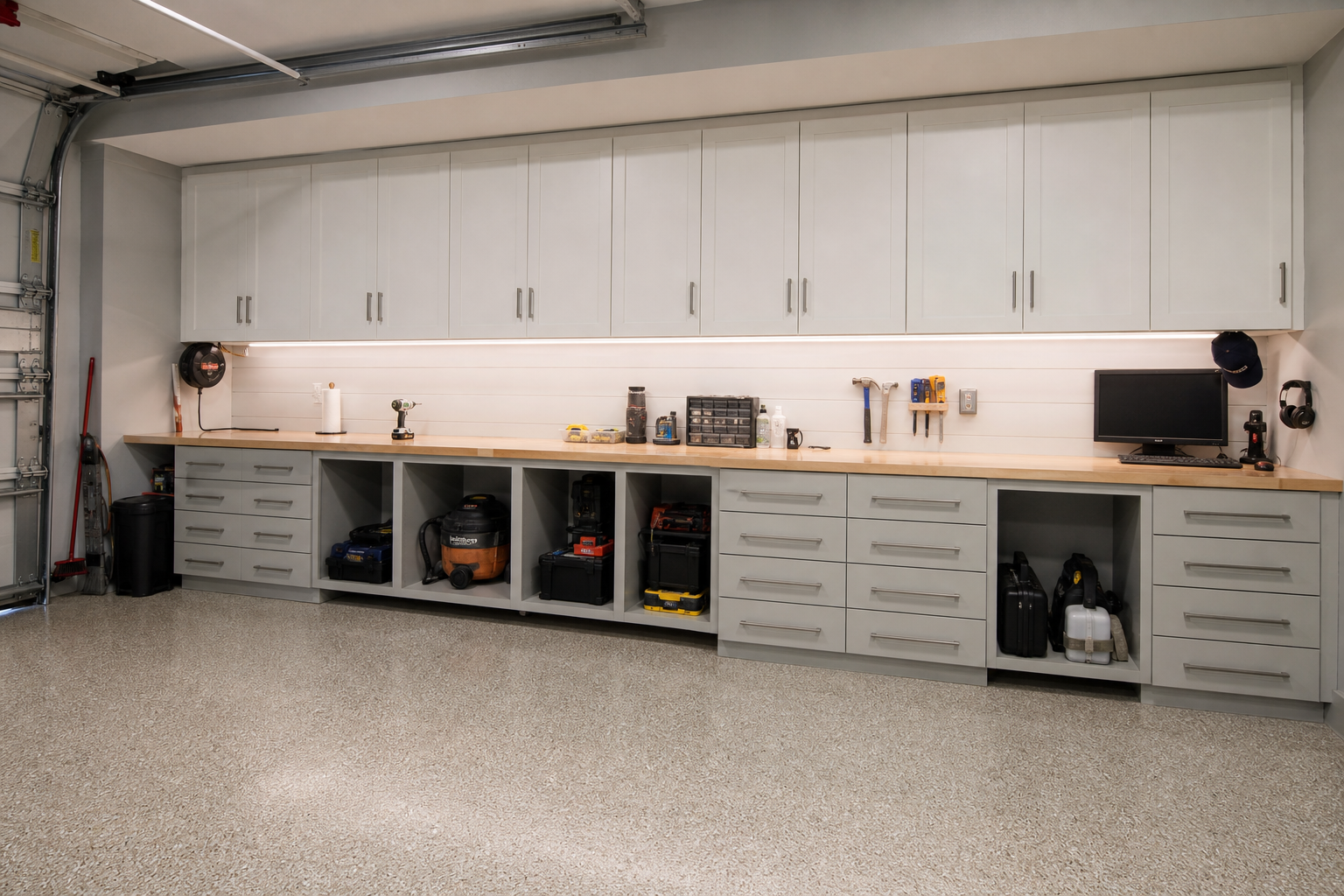 Full-wall built-in garage workbench with oak butcher block top and white shaker upper cabinets