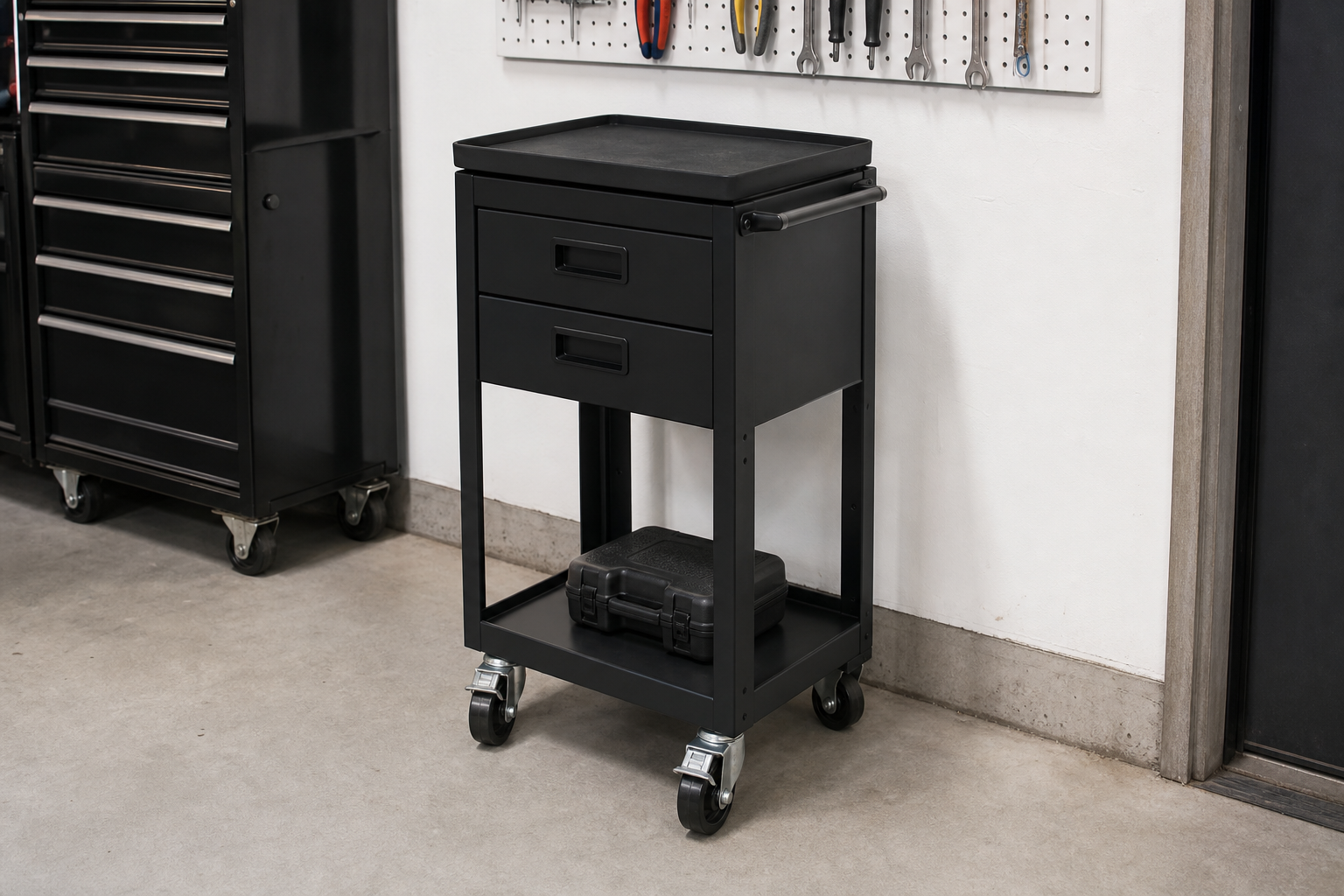 Narrow matte black mobile workbench cart with rubber top and two drawers beside garage wall