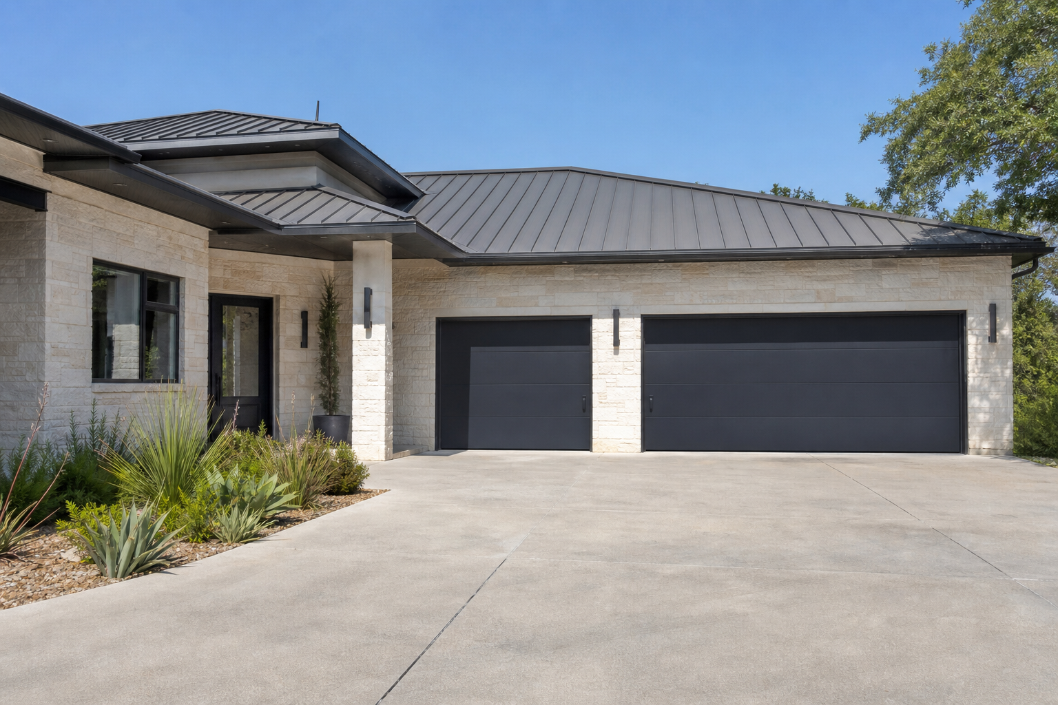 Dark charcoal grey flush panel garage doors with minimalist hardware on limestone facade modern home