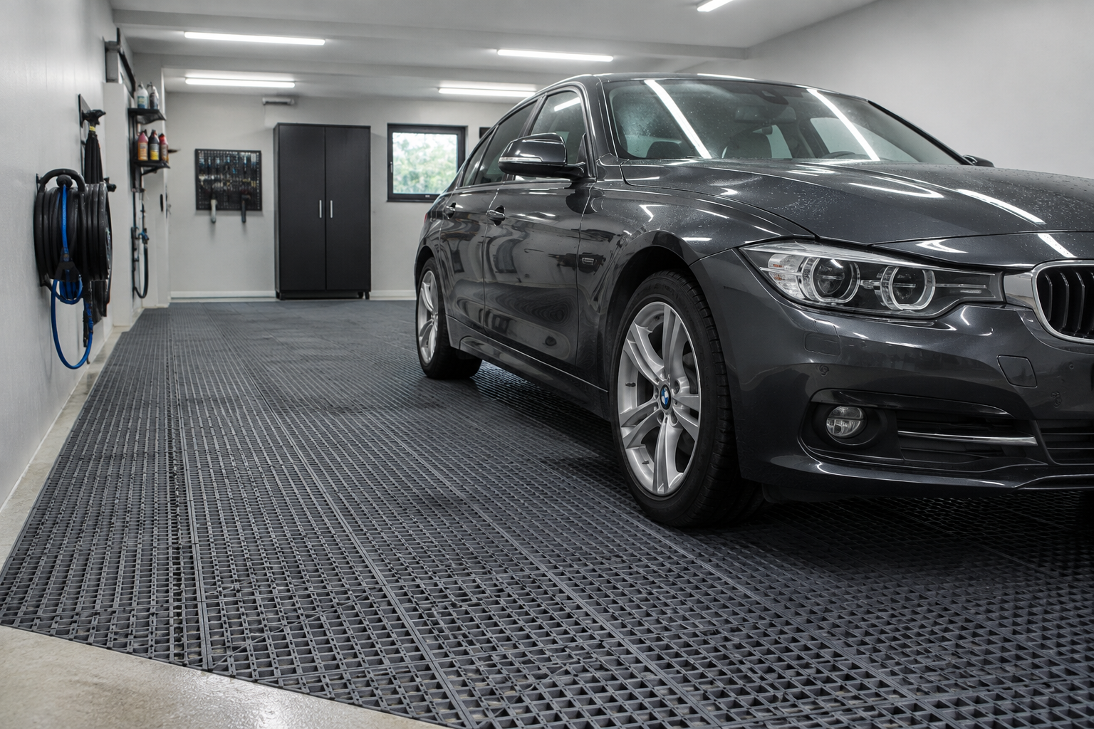 Dark gray interlocking rubber drainage mat tiles on garage floor under car tires in wash bay