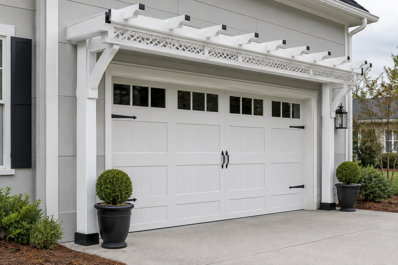 White aluminum pergola with lattice infill panels over a white carriage-style garage door with black decorative hardware