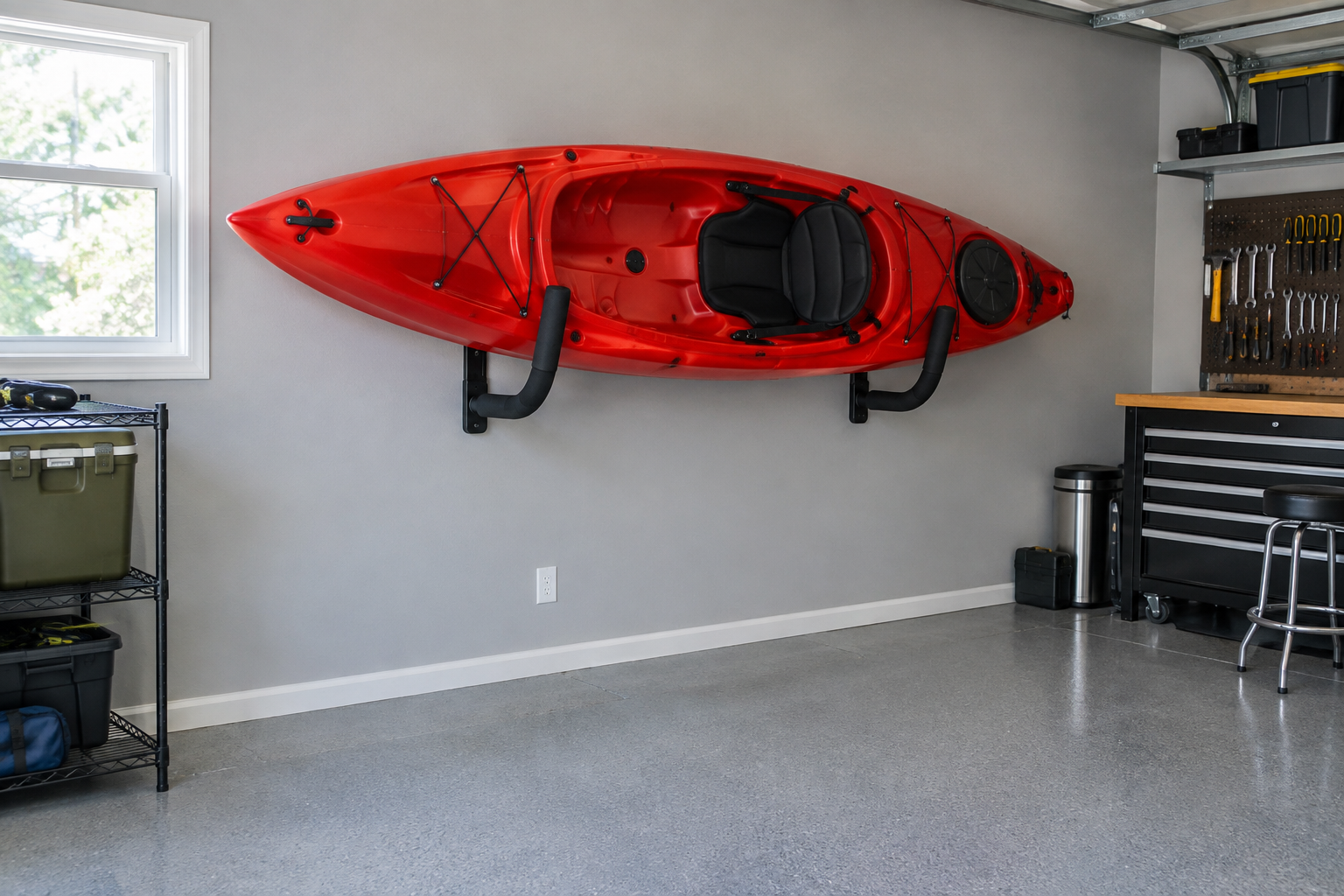 Red sit-on-top kayak stored on black J-style padded wall cradles in a gray painted garage